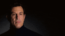 a man is wearing a black turtleneck and looking at the camera