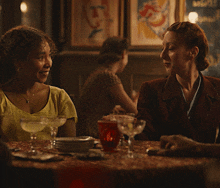 two women are sitting at a table drinking from glasses