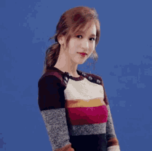 a woman wearing a striped sweater with buttons on the sleeves is standing in front of a blue background .
