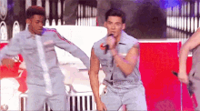 a man is singing into a microphone while two other men are dancing around him .