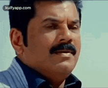 a man with a mustache is making a funny face and looking at the camera .