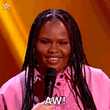 a woman in a pink shirt is holding a microphone and saying aw !