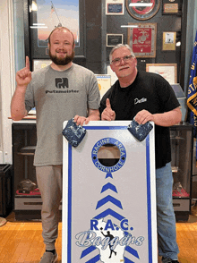 two men are standing next to a cornhole board that says r.a.c. bogeys