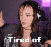 a woman wearing headphones and a choker is sitting in front of a microphone and saying tired af .