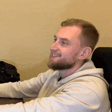 a man with a beard wearing a white hoodie is smiling
