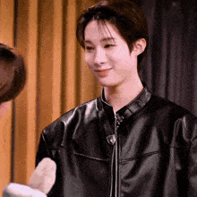 a young man wearing a black leather jacket is smiling while standing next to another man .
