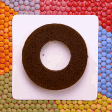 a chocolate cake with a hole in the middle sits on a white plate surrounded by colorful candies