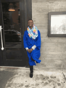 a man in a blue graduation cap and gown stands in front of a door that says " yeh "