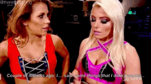 two women are standing next to each other and talking . one of the women is wearing a red top .