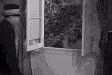 a black and white photo of a man in a hat looking out of an open window .