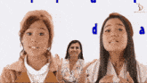 three girls are clapping in front of a white background with the letters d and a