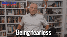 a man in a white shirt is sitting in front of a bookshelf with the words " being fearless " on the bottom