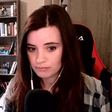 a woman wearing headphones and a plaid shirt is sitting in front of a microphone in front of a bookshelf .