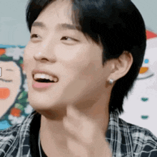 a young man wearing a plaid shirt and earrings smiles