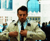 a man in a trench coat and tie adjusts his tie