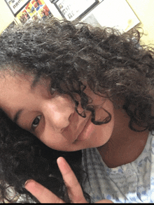 a young girl with curly hair is giving the peace sign