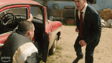 a man in a suit and tie is standing next to another man in a red car with the word prime on the bottom right corner