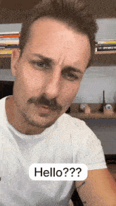a man with a mustache is wearing a white t-shirt and says hello