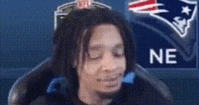 a man with dreadlocks is sitting in front of a patriots logo .