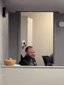 a man behind a counter with a bottle of hand sanitizer in front of him and a thermostat on the wall behind him