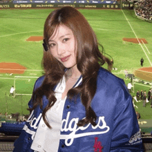 a woman wearing a dodgers jacket stands in front of a baseball stadium