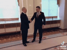 two men in suits shaking hands in a room with a tik tok watermark