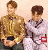two men are sitting next to each other and one of them is petting the other 's head .