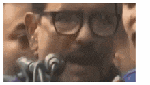 a man with glasses is speaking into a microphone .