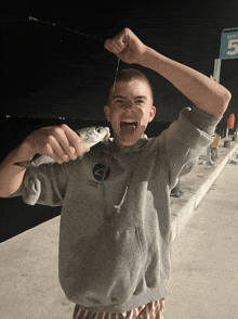 a boy wearing a hoodie that says snow goose on it holds a fish