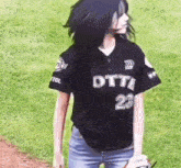 a woman in a black baseball jersey is standing on a baseball field holding a baseball glove .