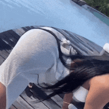 a woman in a white dress is kneeling on a wooden deck next to a pool