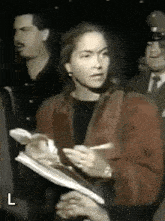a woman in a red jacket is writing on a piece of paper in front of a man in a black shirt and tie ..