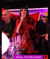 a woman in a red dress sits at a table with wine glasses and the words albania 11th of 26 countries on the screen