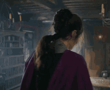 a woman in a purple cape stands in a room