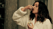 a woman in a white robe is drinking a shot of tequila