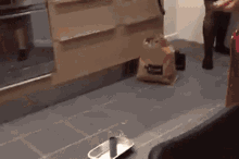 a person is standing in a kitchen with a bag on the floor and a tray on the floor .