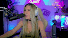 a woman wearing headphones stands in front of a microphone in front of a sign that says ' twitch ' on it