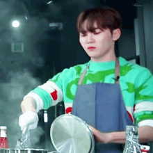 a man wearing an apron and a green sweater is cooking in a kitchen