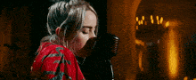 billie eilish is singing into a microphone while wearing a red shirt .