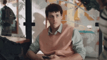 a man wearing a pink vest is sitting at a table looking at his phone