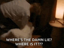a man is laying on a bed with a pillow and a lamp and says where 's the damn lie ?