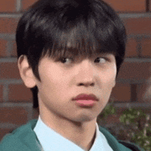 a young man in a green jacket and white shirt is making a funny face in front of a brick wall .