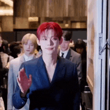 a man with red hair is wearing a blue suit and waving while standing in front of a door .