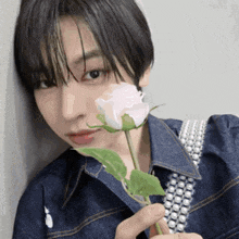 a young woman in a denim shirt is holding a pink rose in front of her face