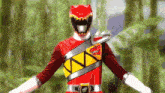 a red power ranger is standing with his arms outstretched in front of a forest