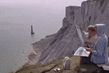 a couple of people sitting on top of a cliff overlooking the ocean
