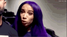 a woman with purple hair is sitting next to a man in a room .