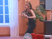 a woman in a black dress is dancing in a living room while holding a glass of wine .