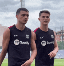 two men wearing black spotify shirts stand next to each other