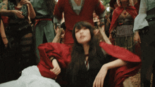 a woman in a red dress is surrounded by people